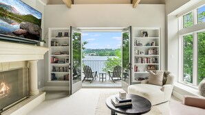 Een ruime woonkamer met een open haard, een grote televisie en een balkon met buitenmeubilair.