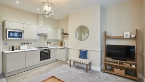 A modern kitchen with built-in appliances, a dining area with a bench, and a TV on a wooden stand. - Host & Stay | Silver Beach (Whitby)