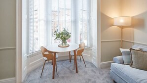 A corner room with a bay window, a round table with chairs, a floor lamp, and a sofa. - Host & Stay | Silver Beach (Whitby)