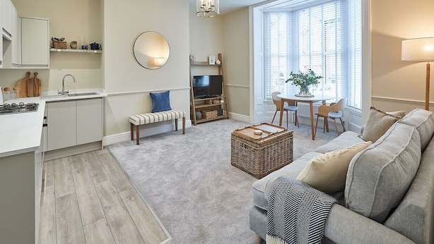 A modern living room with a sofa, a coffee table, and a TV. There is a kitchen area with a sink and cabinets. - Host & Stay | Silver Beach (Whitby)
