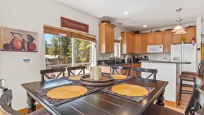 A modern kitchen with wooden cabinets, a dining area with a round table, and a view of the outdoors. - Doc's Place (Leadville)