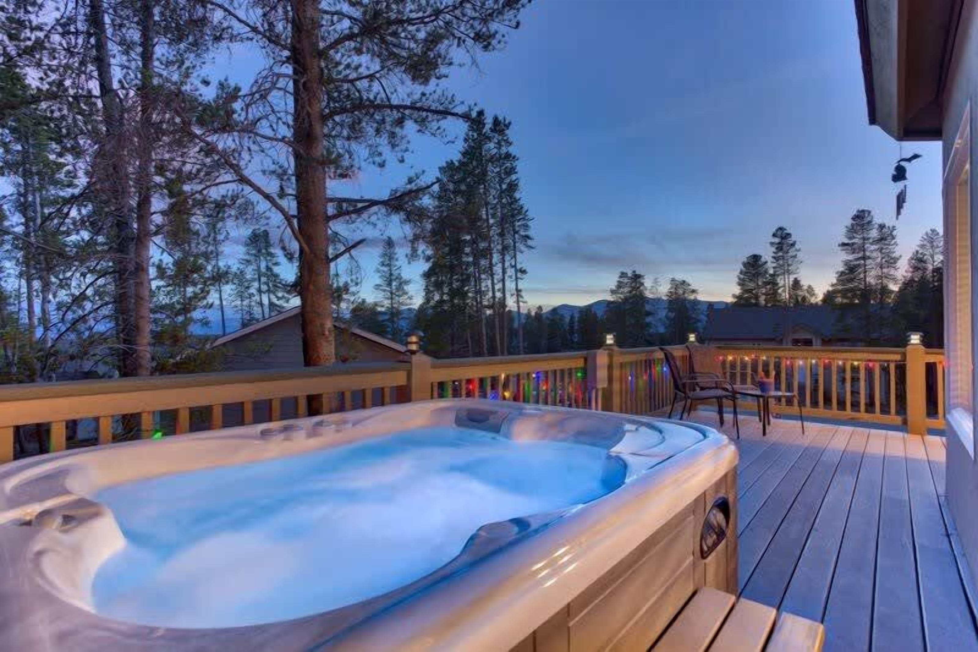 Un jacuzzi en una terraza de madera con vista a árboles y montañas.