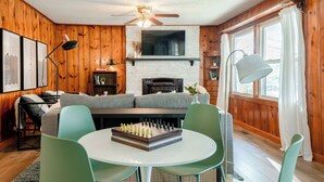 Een gezellige woonkamer met een open haard, houten wanden, een bank en een schaaktafel.