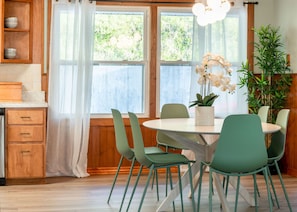 Comedor con una mesa redonda, seis sillas, una orquídea en maceta y un aparador de madera con vajilla.