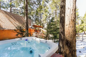 Un jacuzzi en un área boscosa, con un edificio de madera al fondo.