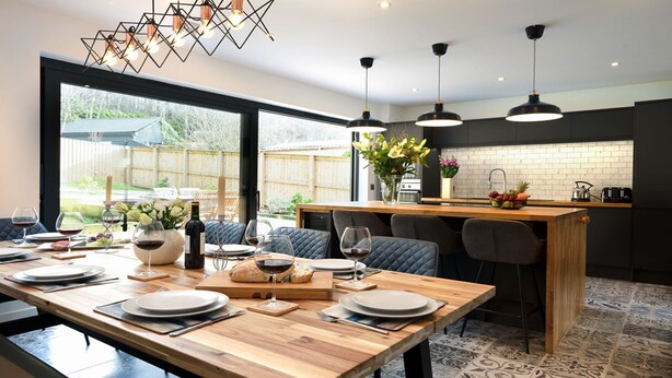 A modern kitchen with a wooden island, black bar stools, and pendant lighting. - Two Queens Houses -  a house that sleeps 10 guests  in 5 bedrooms (Aviemore)
