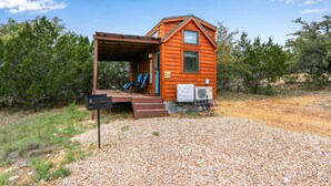 A small wooden cabin with a covered porch, a small window, and a sign indicating it is a motel. - Pet-Friendly Tiny Home in Dripping Springs w/ Hill Country Views (Dripping Springs)