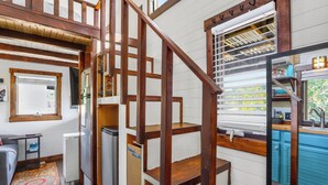 A multi-level wooden staircase connecting different rooms, a kitchen area with blue cabinets, and a small seating area with a sofa and a coffee table. - Pet-Friendly Tiny Home in Dripping Springs w/ Hill Country Views (Dripping Springs)