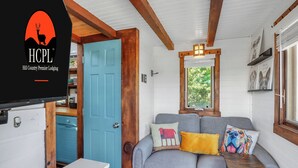 A compact RV interior with a kitchenette, a sofa with decorative pillows, and a window with a view of greenery. - Pet-Friendly Tiny Home in Dripping Springs w/ Hill Country Views (Dripping Springs)