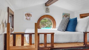 A cozy room with a bed, a wooden bench, and a window with a view of greenery. - Pet-Friendly Tiny Home in Dripping Springs w/ Hill Country Views (Dripping Springs)