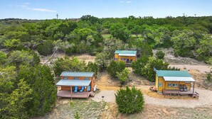 A remote, rustic cabin area with multiple cabins surrounded by dense greenery. - Cozy Tiny House in Dripping Springs w/ Sunset Views & Romantic Fireplace (Dripping Springs)