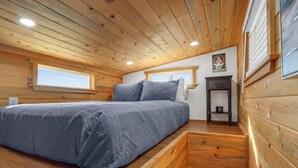 A bedroom with a bed, wooden walls, a window, and a small shelf. - Cozy Tiny House in Dripping Springs w/ Sunset Views & Romantic Fireplace (Dripping Springs)
