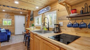 A cozy kitchen with wooden walls, a stainless steel sink, a coffee maker, and a sign that reads "OUR HAPPY PLACE". - Cozy Tiny House in Dripping Springs w/ Sunset Views & Romantic Fireplace (Dripping Springs)
