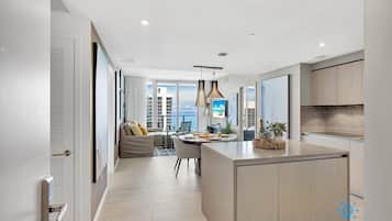 A modern kitchen with a central island, a dining area with a table and chairs, and a view of the city through large windows.
