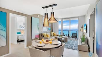 A modern hotel room with a dining area, a balcony with a view of the sea, and a large window.