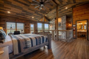 Un dormitorio amplio con una cama grande, techo de madera, pared de piedra y vistas al exterior.