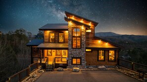 Una baita in legno a due piani con facciata in pietra, ampie finestre e un portico con ringhiera.