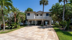 A two-story house with a covered porch and a driveway. - 295 Ostego Dr - Gorgeous Bay Front Home 4 Bedroom Home by RedAwning (Fort Myers Beach)