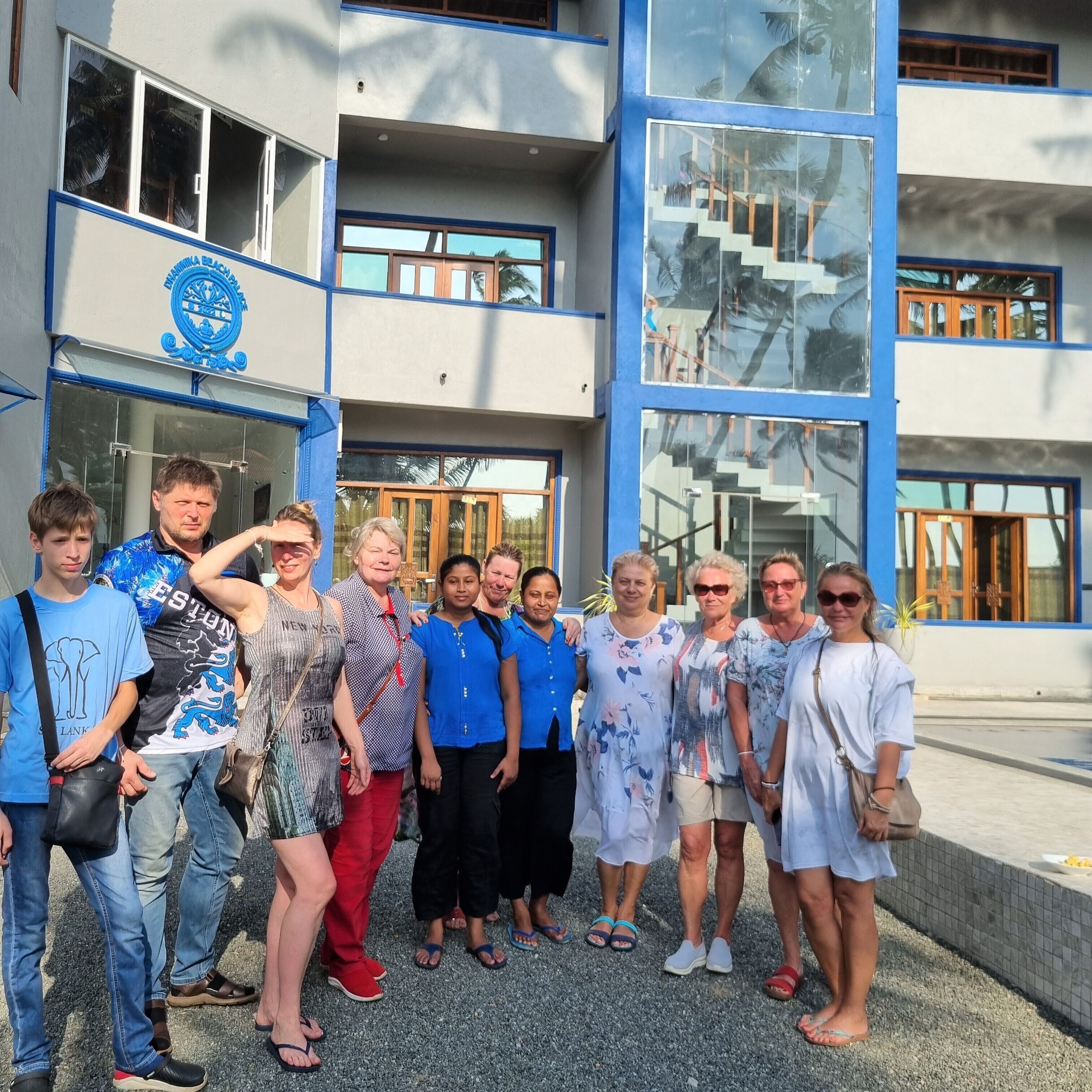 A group of people posing in front of a building with a blue and white color scheme, featuring large windows and a staircase.
