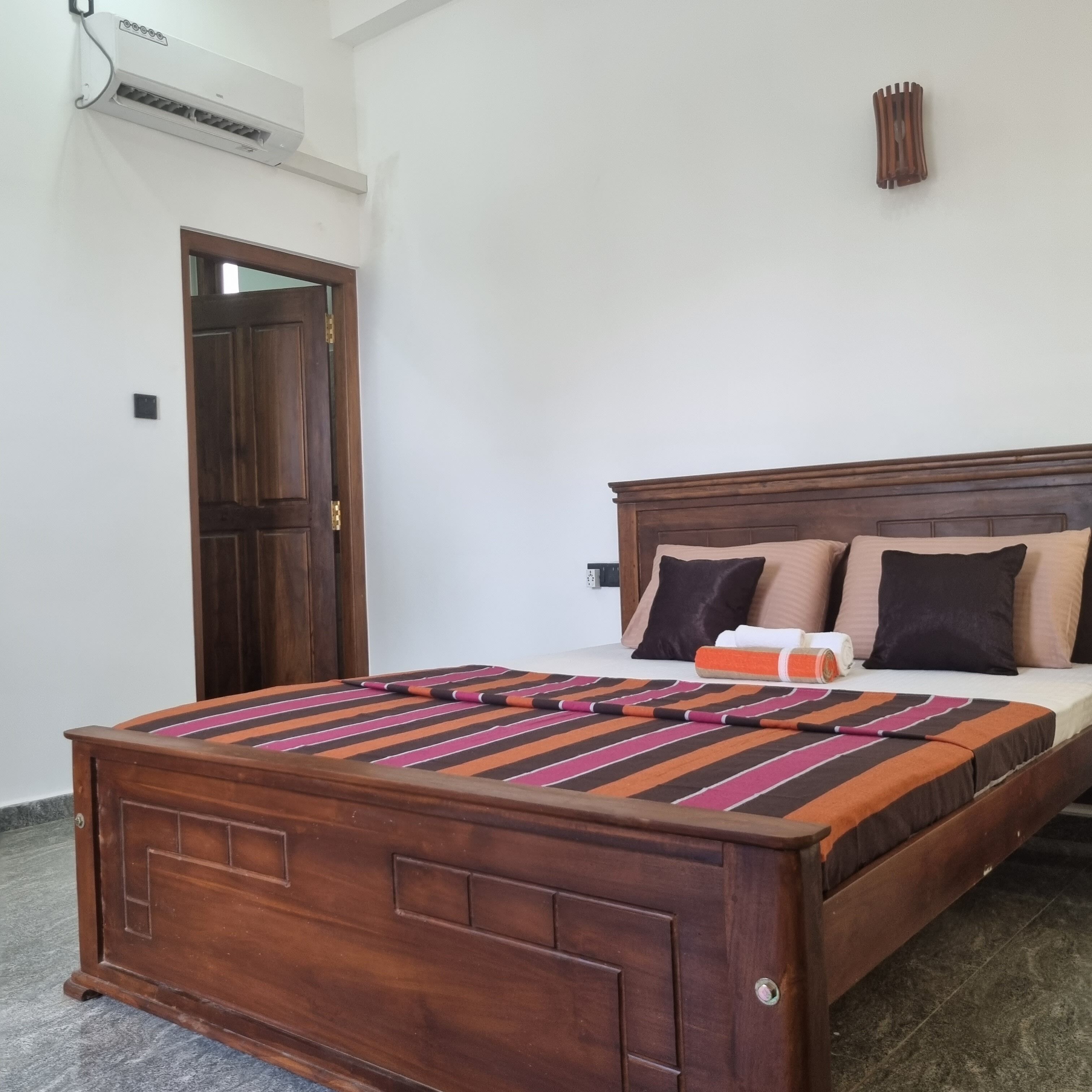 A wooden bed with a striped bedspread, a wooden headboard, and a wall-mounted air conditioner.