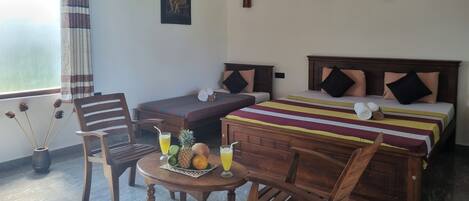 A hotel room with two single beds, a wooden table with fruits and a drink, a chair, and a window with curtains.