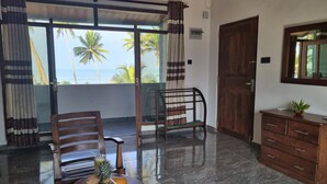 A room with a dining table set with fruits and a drink, a wooden chair, a wooden cabinet, and a view of the ocean through large windows. - Dhammika Beach Palace (Wadduwa)