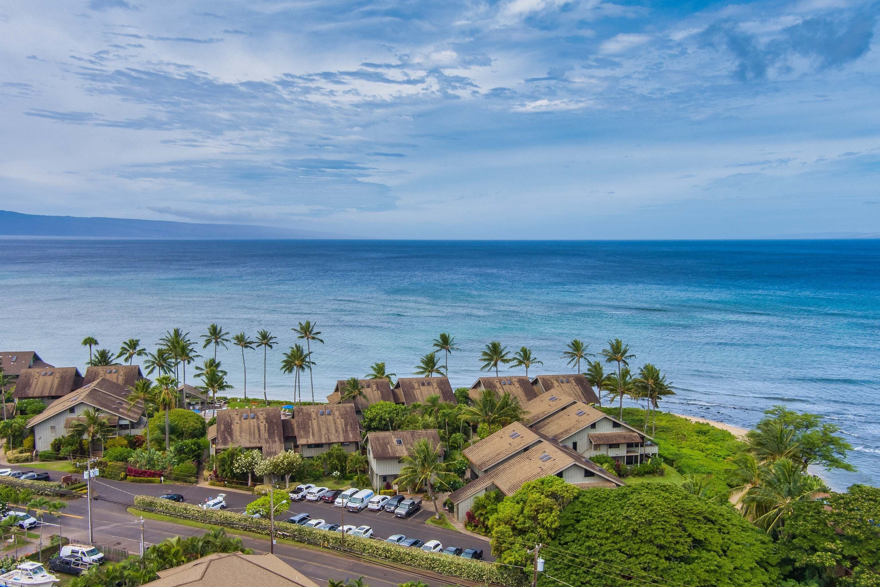 A coastal village with thatched-roof houses, a parking lot, and a view of the ocean.