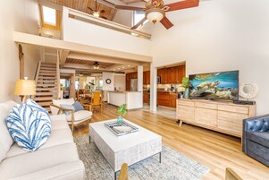 Amplia sala de estar con techo alto, piso de madera, una escalera que conduce a un nivel superior y una cocina con armarios de madera.
