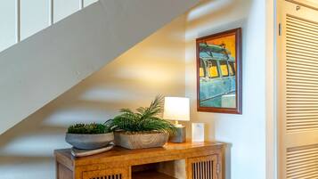 A wooden console table with a potted plant and a lamp, a painting of a vintage car on the wall, and a staircase in the background.