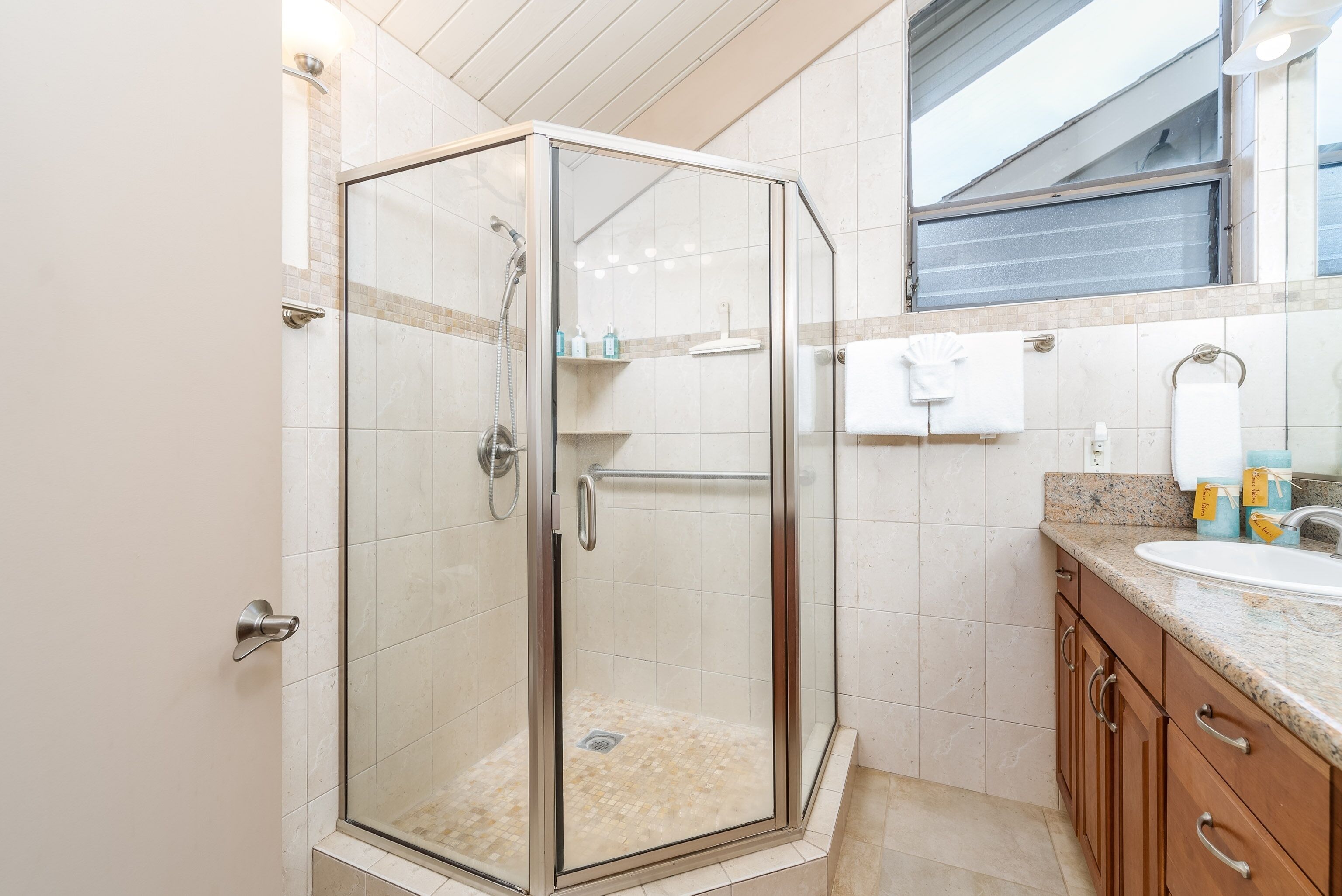 A glass-enclosed shower with a tiled floor, a sink with a granite countertop, and wooden cabinets.