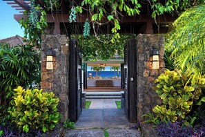 Step into a tranquil beachfront retreat, where lush tropical plants surround a covered seating area beneath a stone archway.