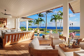 Relax in style with a sofa, chairs, and table on the spacious deck, offering a view of the ocean and palm trees.