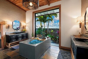 Bathroom features a large bathtub, vanity, and sink, with a window offering a view of palm trees.