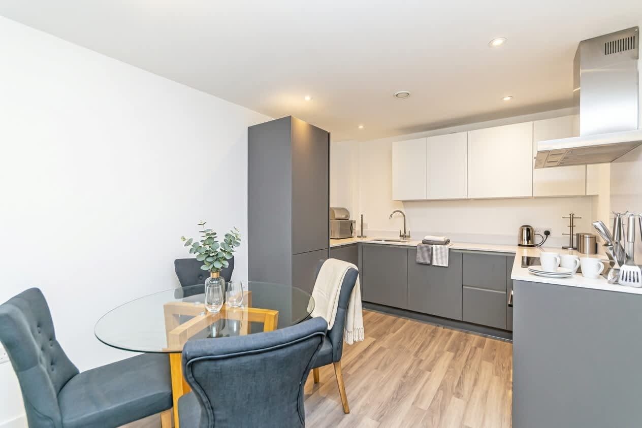 A modern kitchen with a central island, white cabinets, and a dining area with a glass table and chairs.