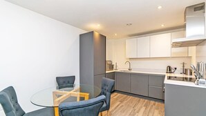 A modern kitchen with grey cabinets, a stainless steel range hood, and a glass dining table with four chairs. - Central Manchester 2BR Apartment + Free Parking (Manchester)
