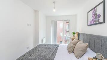 A bedroom with a bed, a bedside table, a lamp, and a window with a view of buildings.