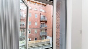 A view through a window of a multi-story building with balconies and a wooden deck. - Central Manchester 2BR Apartment + Free Parking (Manchester)