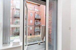 A balcony with a view of a brick building, a white towel, and a mug on the floor. - Free Parking | 2BR Apartment in Central Manchester (Manchester)