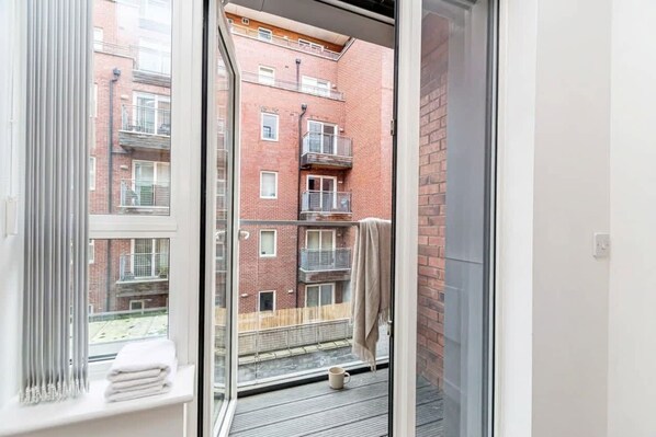 A balcony with a view of a brick building, a white towel, and a mug on the floor. - Free Parking | 2BR Apartment in Central Manchester (Manchester)