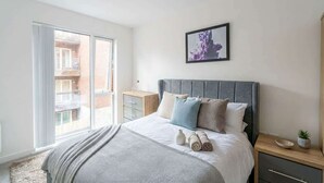 Une chambre à coucher avec un lit, une table de chevet, une commode, une fenêtre et un tableau encadré au mur.