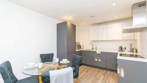 Une cuisine moderne avec des meubles gris, une hotte en acier inoxydable et un coin repas comprenant une table en verre et des chaises grises à revêtement.