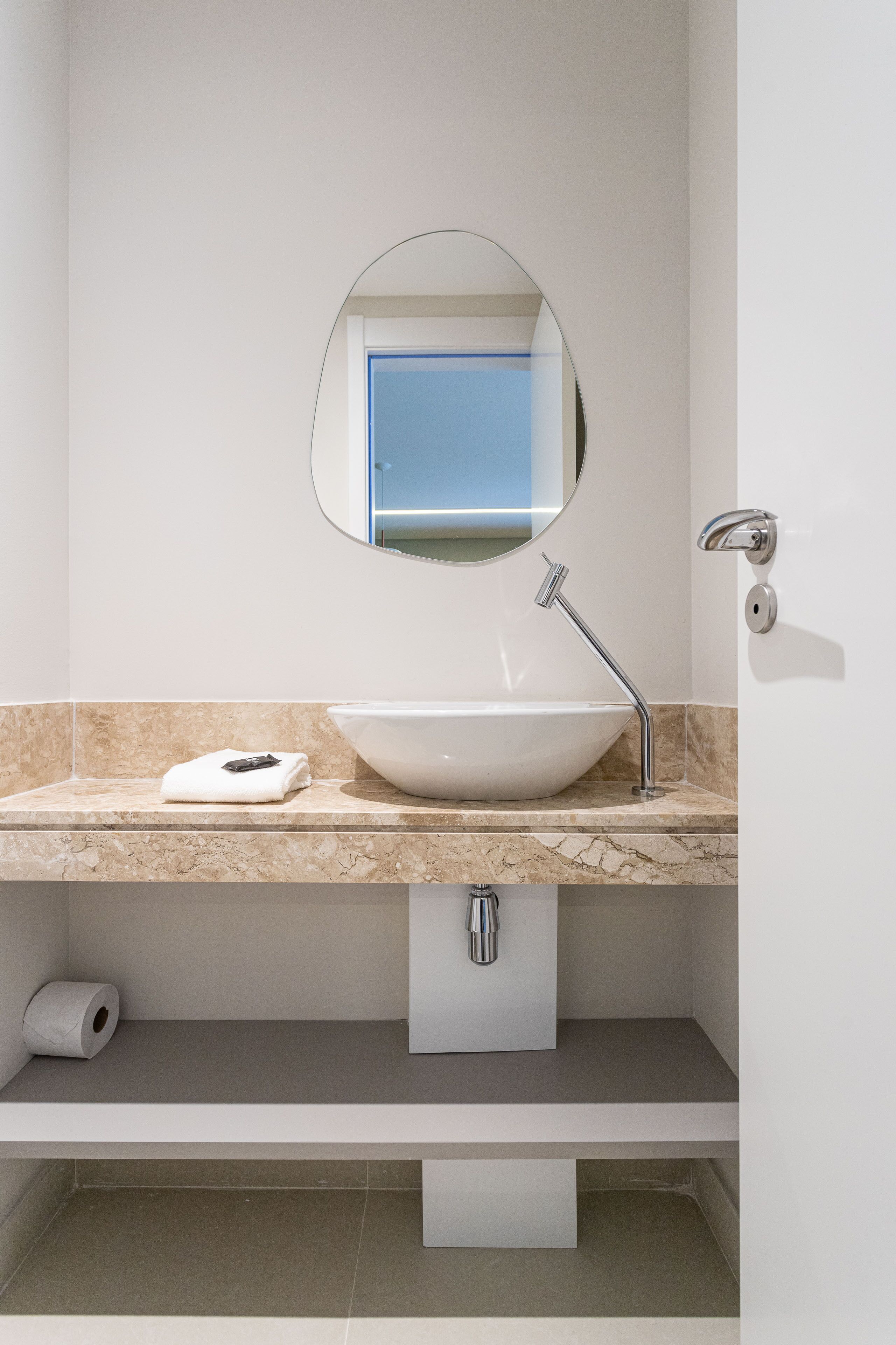 Ein modernes Badezimmer mit einem weißen Waschbecken, einem runden Spiegel und einem Handtuch auf der Ablagefläche.
