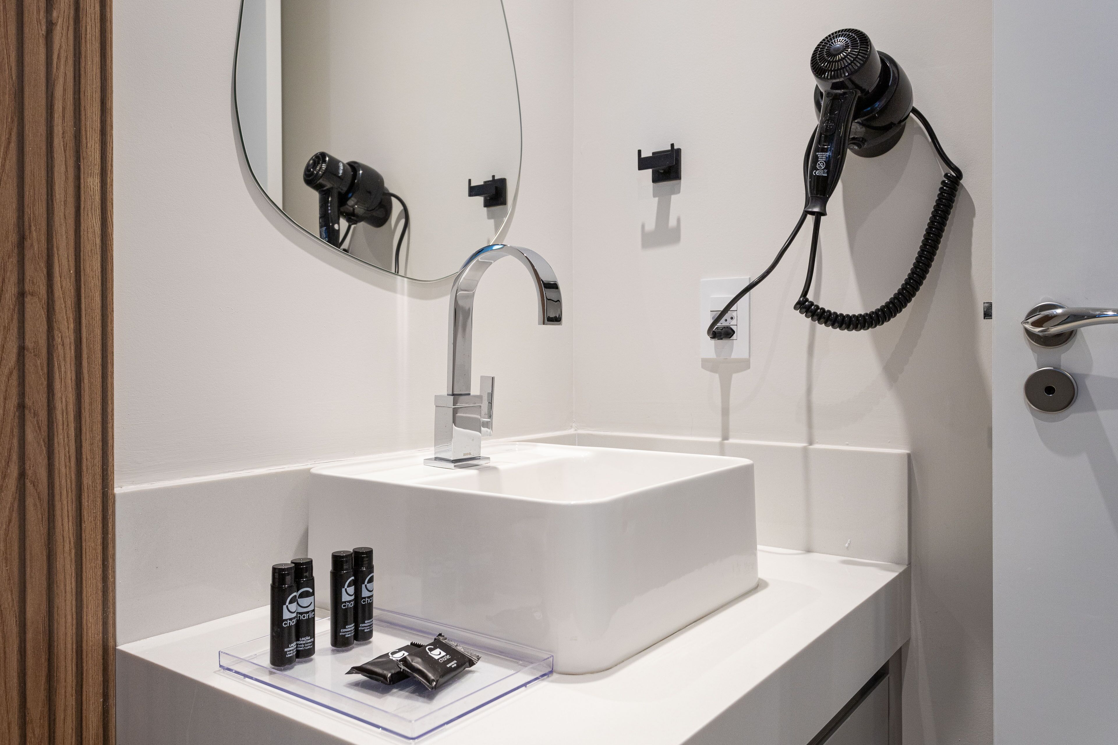 A bathroom with a white sink, a mirror, a hairdryer, and two hair care products on the counter.