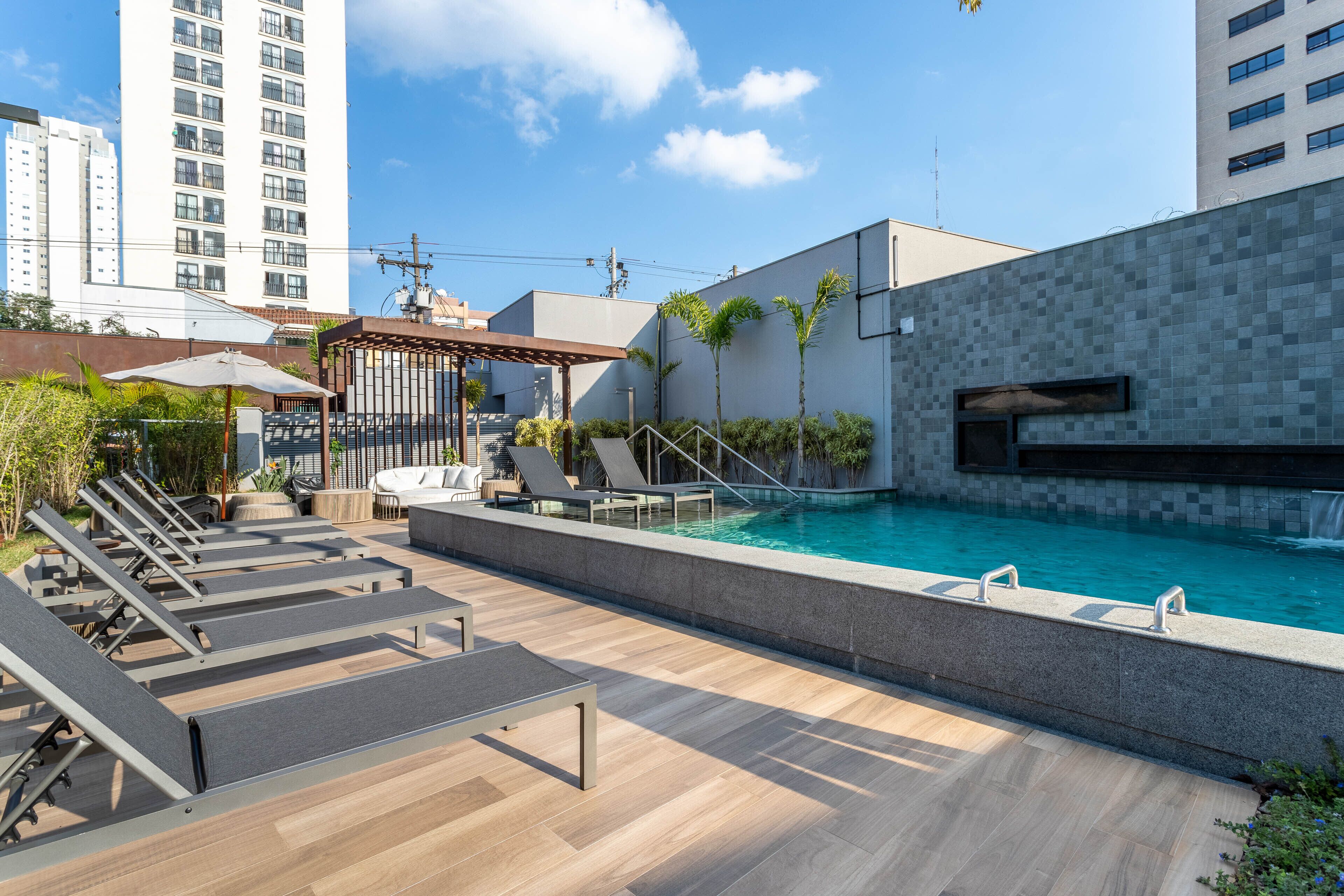 A rooftop pool area with lounge chairs, a pergola, and a small waterfall feature.