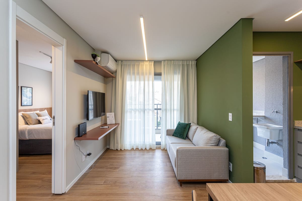 Un apartamento moderno con piso de madera, un sofá, una televisión, una mesita y un baño visible a través de una puerta abierta.