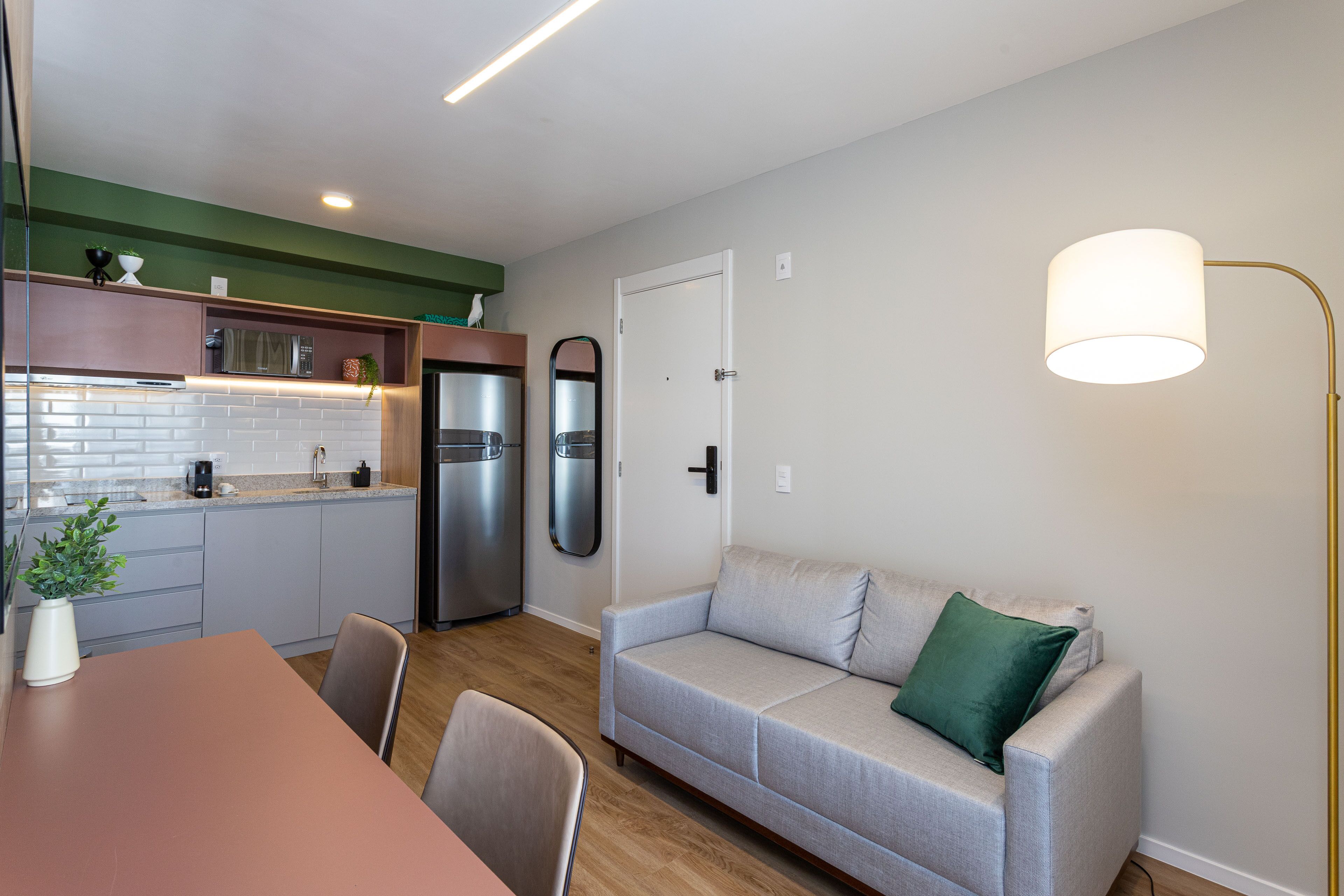 A compact living space with a kitchenette, a dining area, and a sofa with a green pillow.