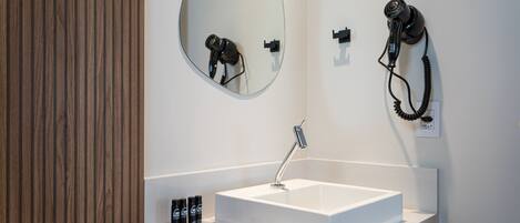 A modern bathroom with a white sink, a mirror, and a hairdryer mounted on the wall.