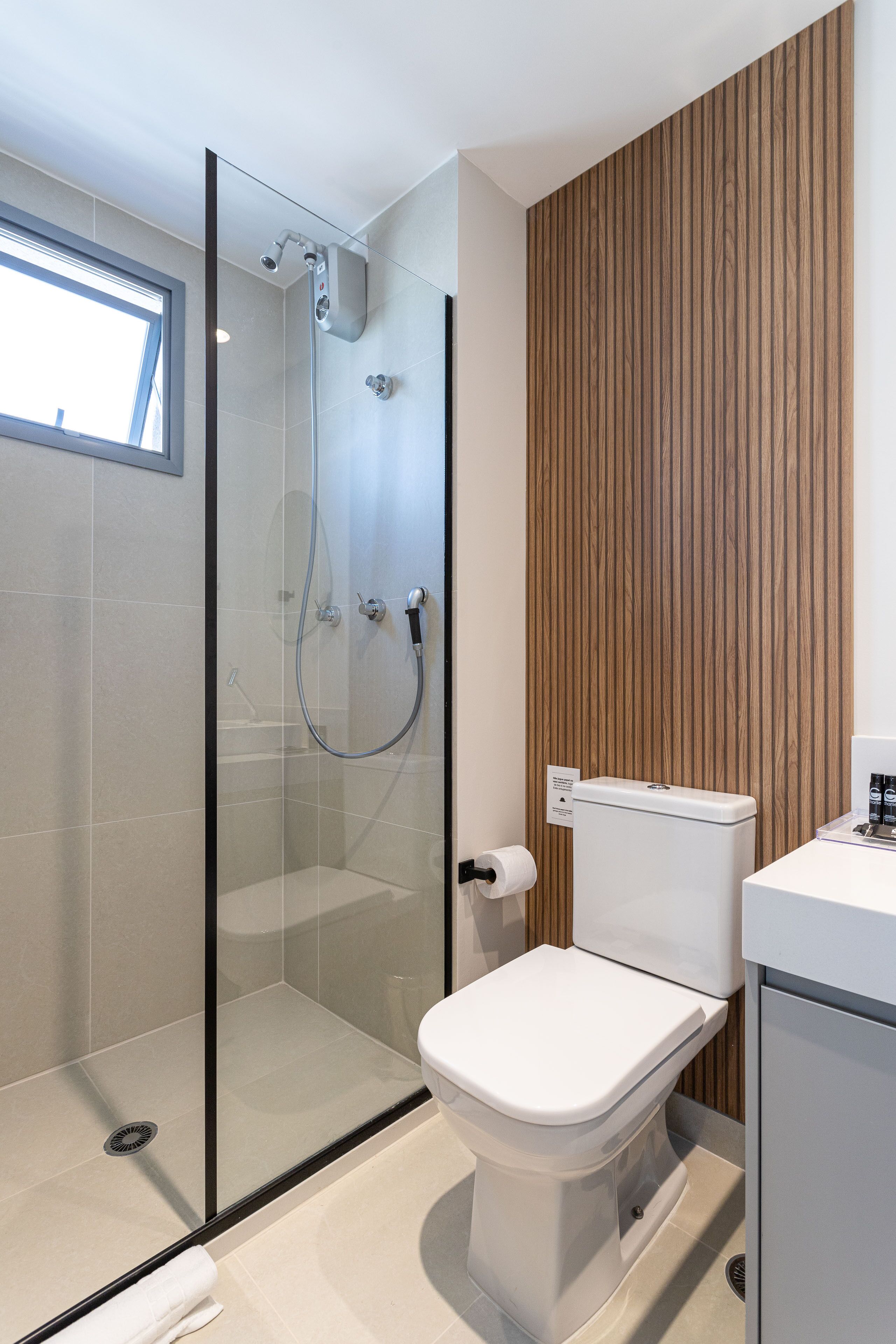 A modern bathroom with a glass-enclosed shower, a toilet, and a wooden panel wall.