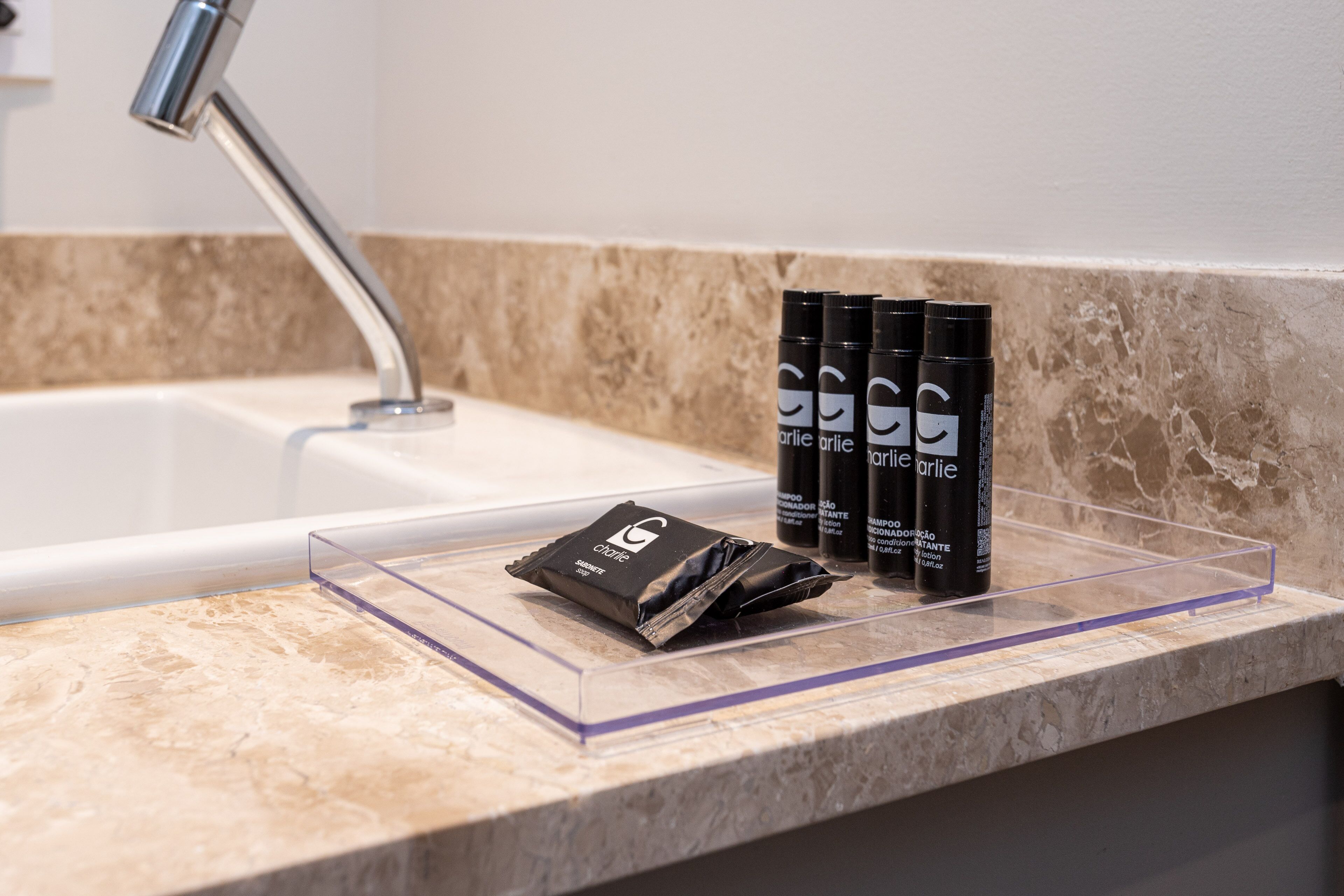 A bathroom counter with a marble sink, a faucet, and three bottles of Charlie perfume.