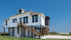 Une maison à deux étages avec un balcon, un escalier et une vue sur la plage.